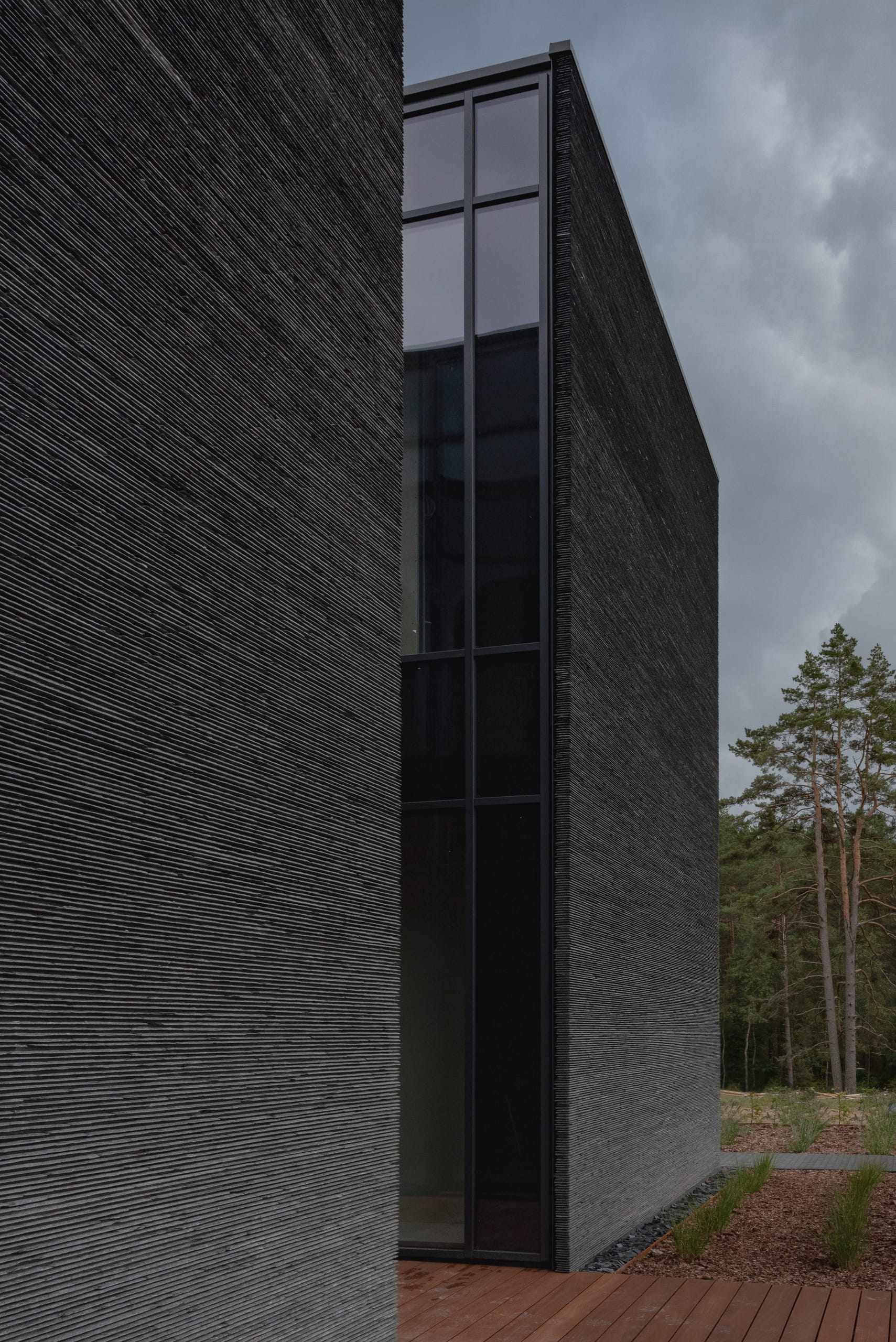 IN JAN House — narrow glazed slot between its two stone volumes under a grey sky