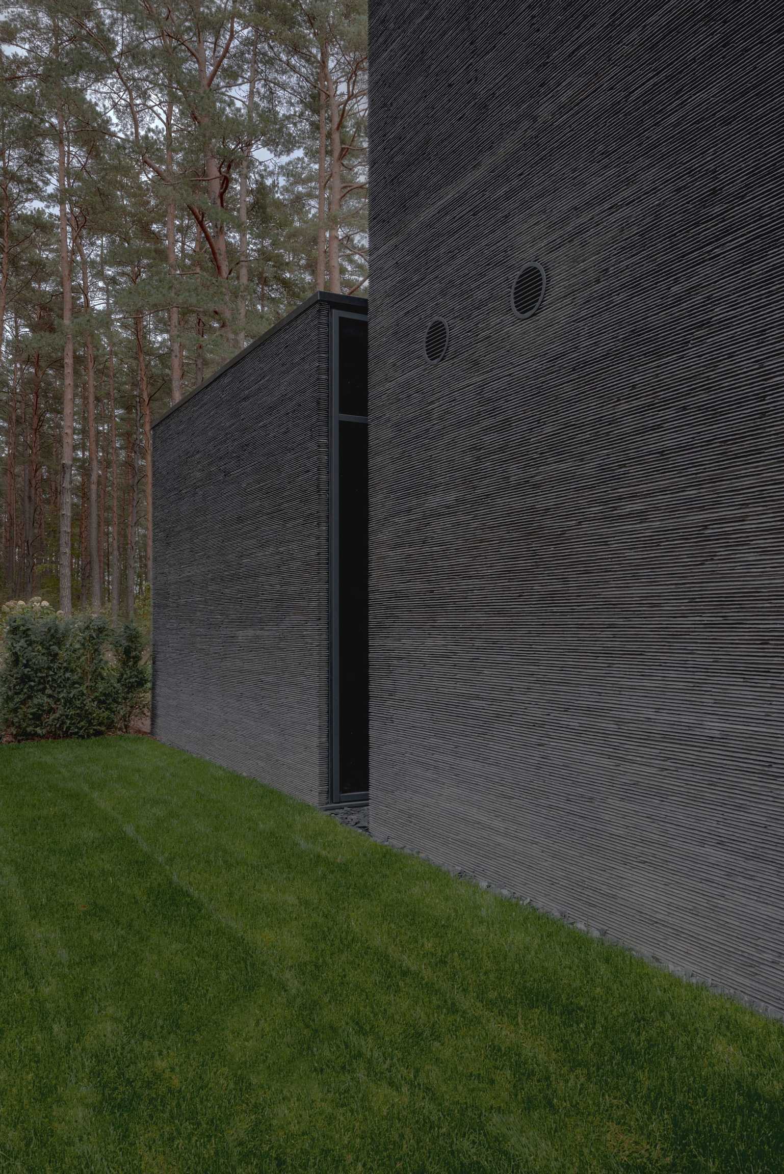 IN JAN House — textured stone facades meeting a mown lawn, pines beyond