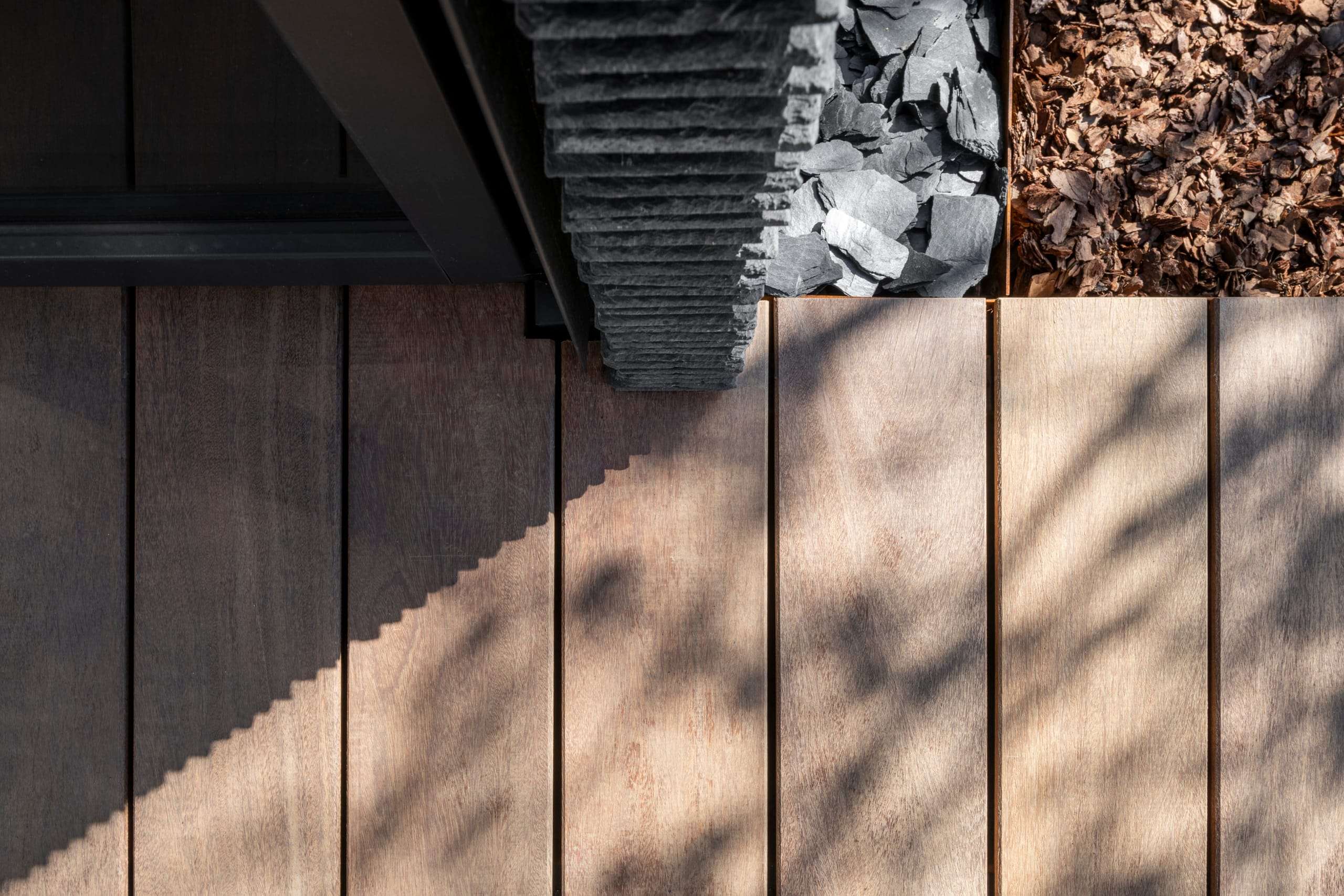 IN JAN House — timber decking meeting slate chippings in the shadow of the eaves
