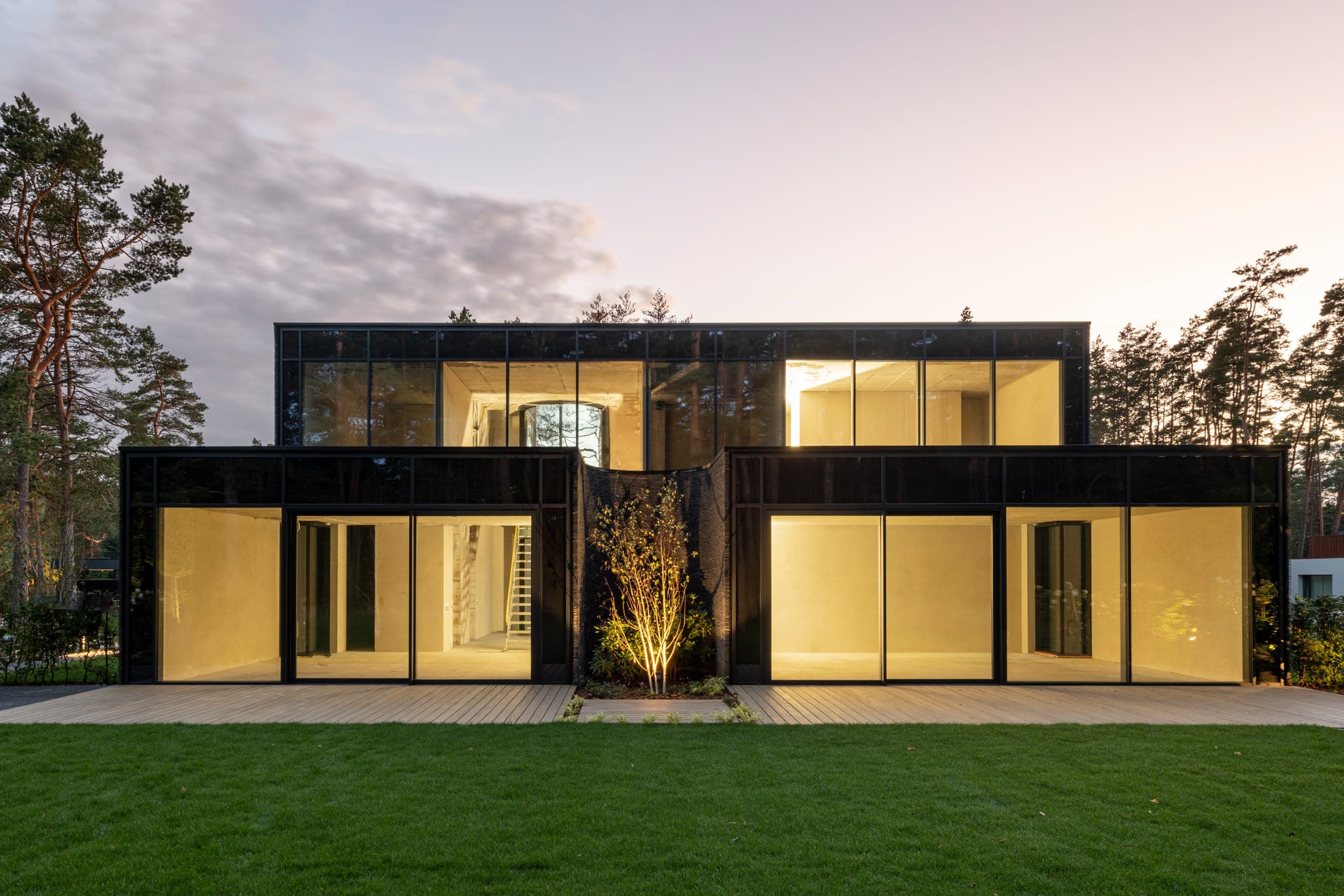 IN JAN House — at dusk, glazed ground floor glowing beneath the dark upper volume