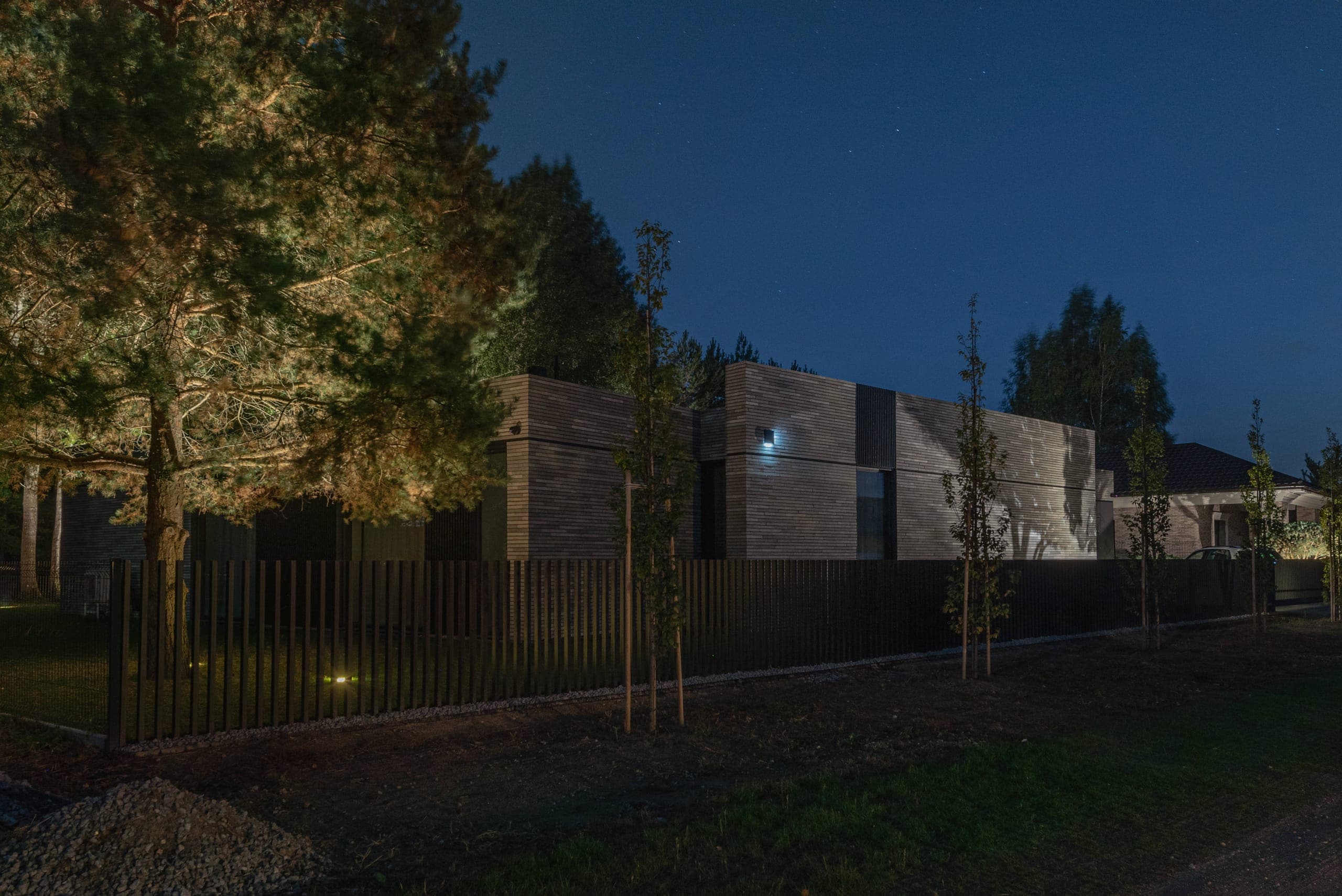 Modern Family House — at night behind its timber fence, lit from the garden