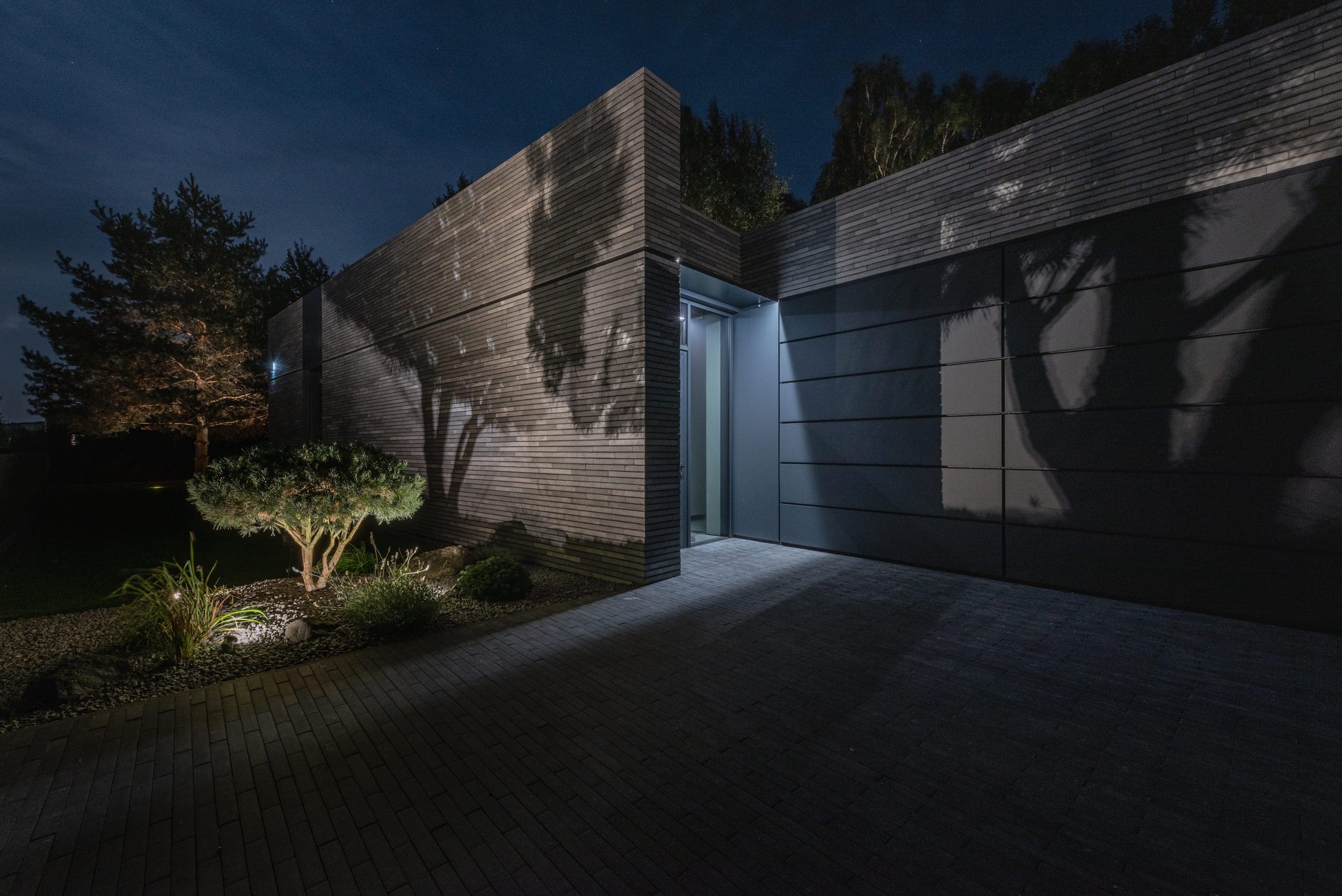 Modern Family House — lit entrance recessed between brick and dark panelled walls at night