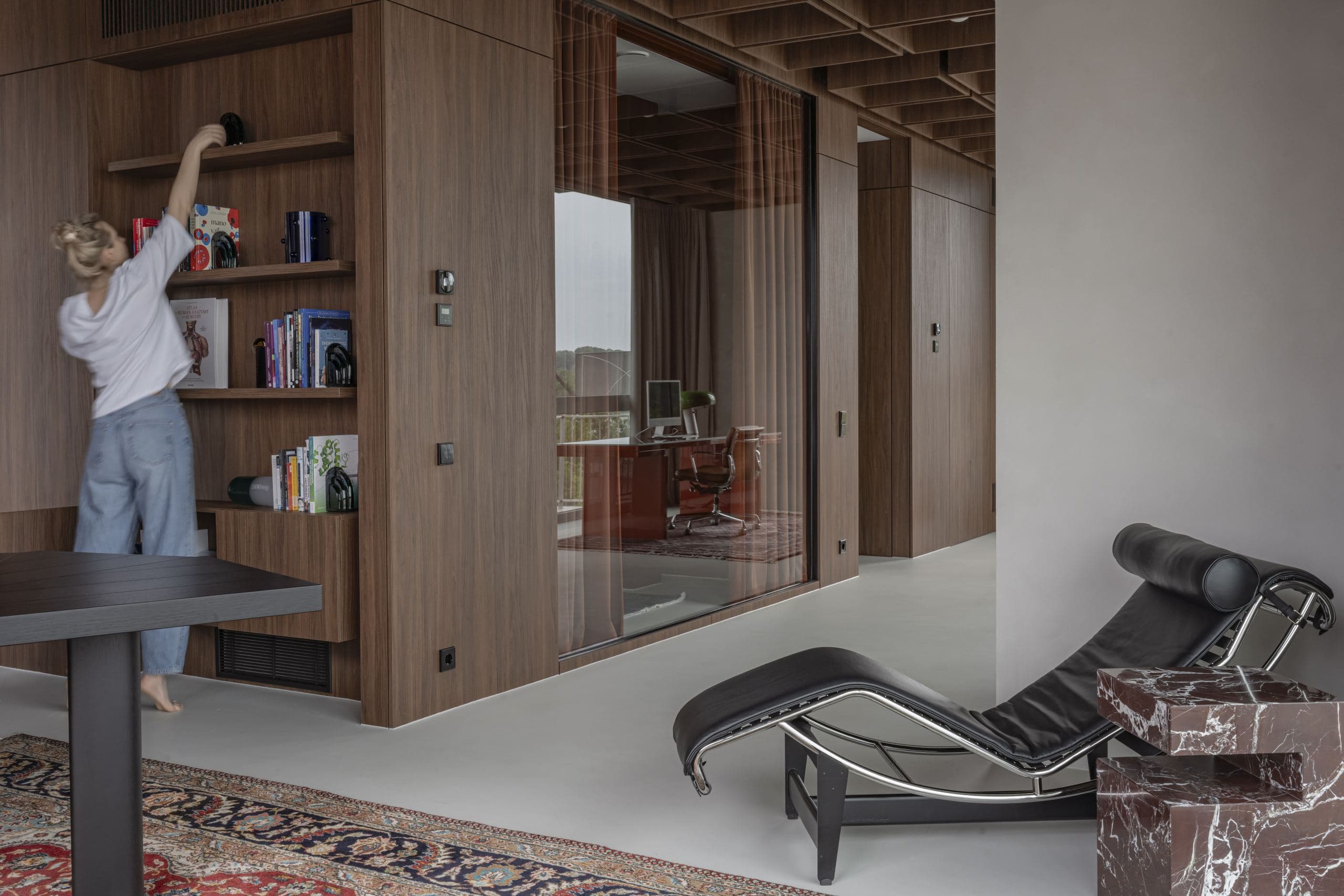 Bespoke Office Interior — figure stretching beside a leather lounge chair and built-in bookshelf