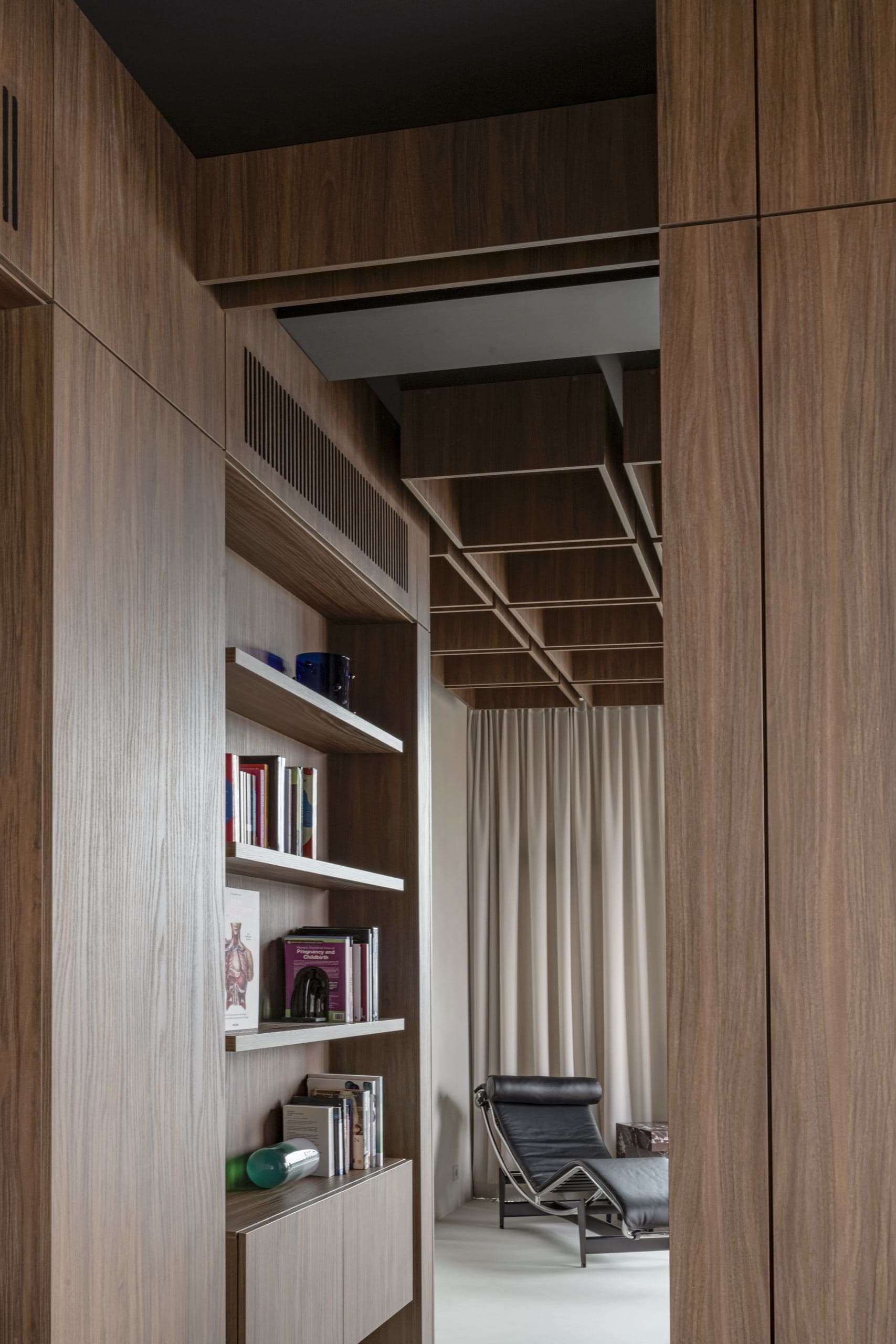 Bespoke Office Interior — walnut shelving and a lounge chair beside draped curtains