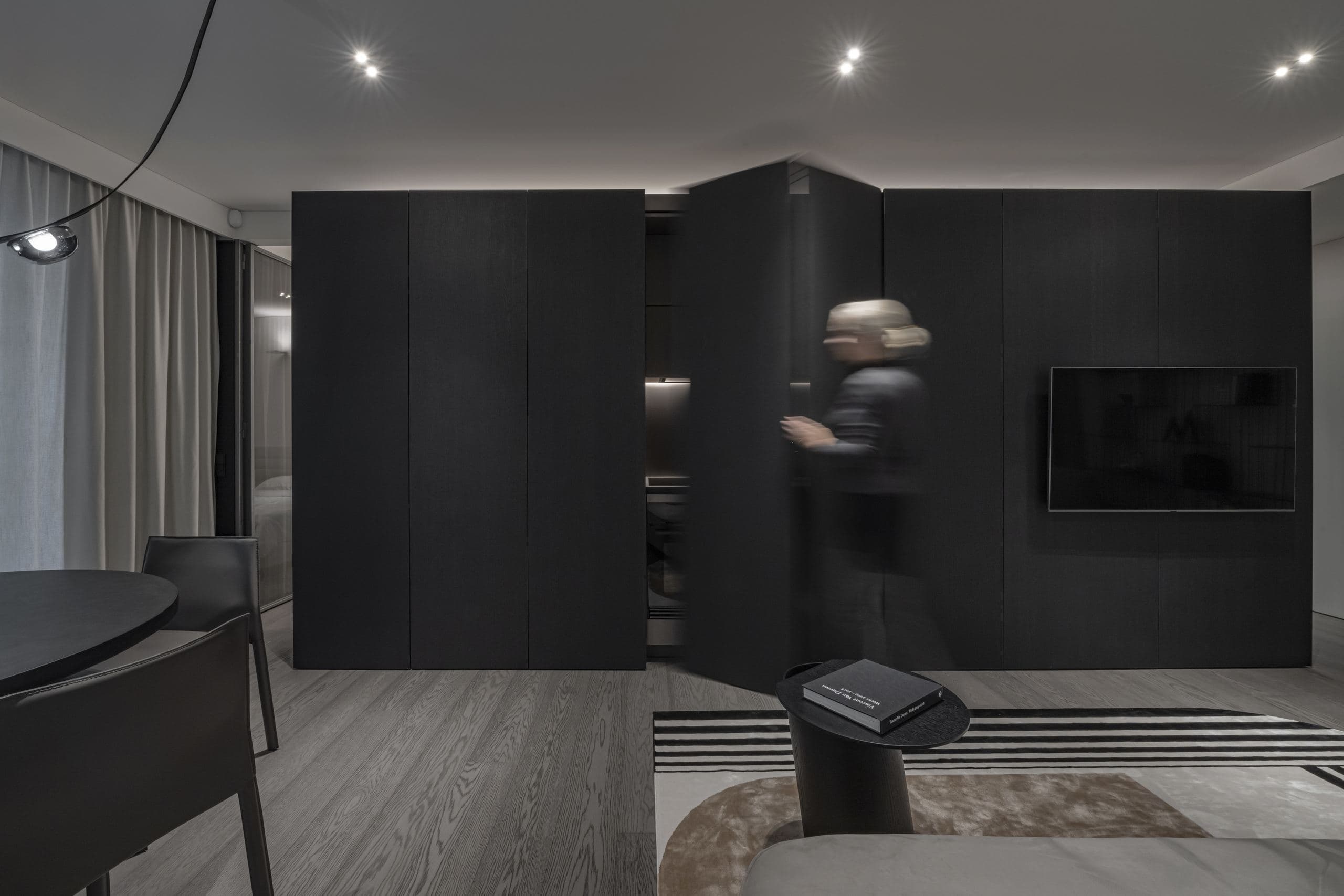 Paupys Apartment — figure caught mid-motion beside the black monolithic volume and television