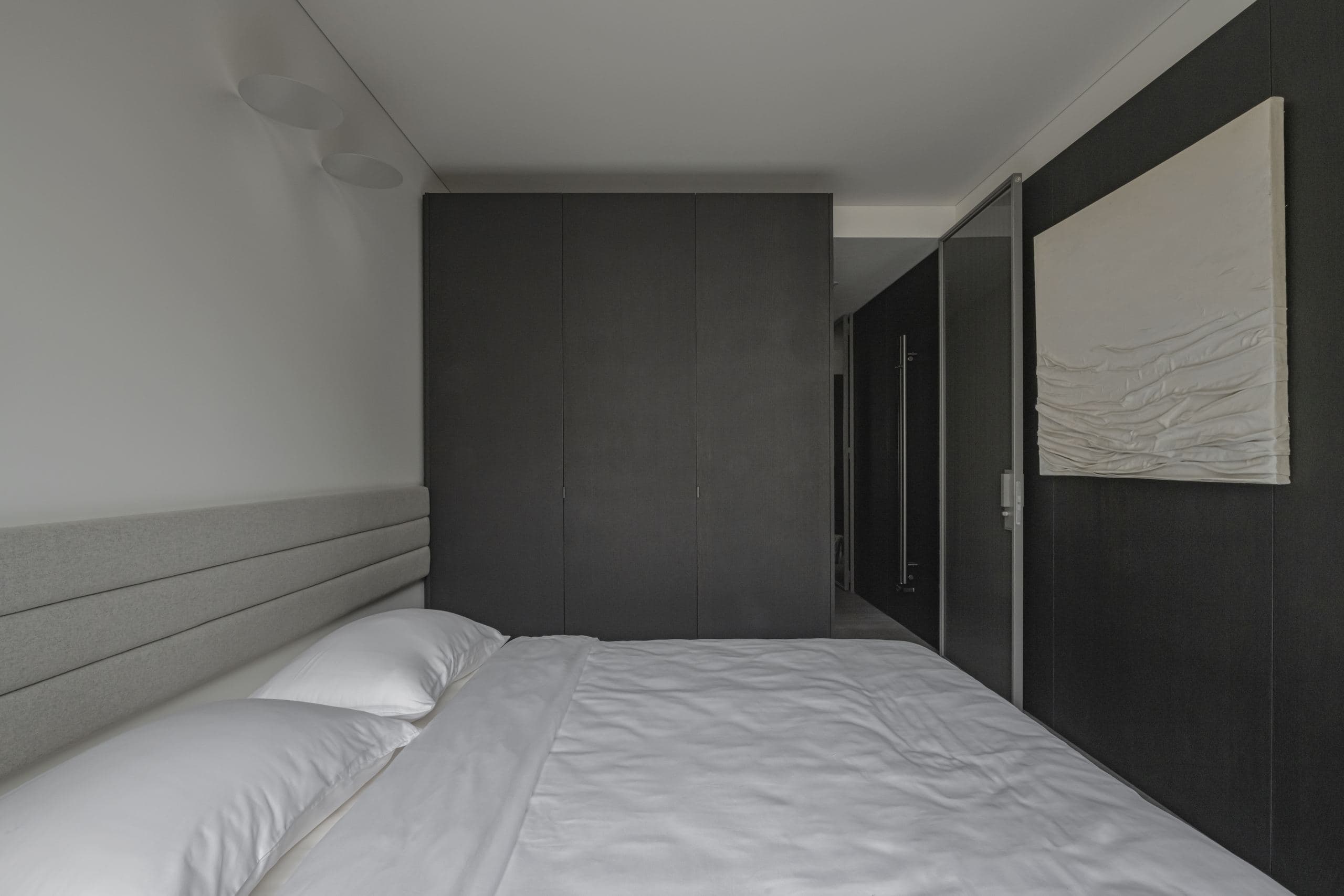 Paupys Apartment — bed against the finely textured black monolithic volume