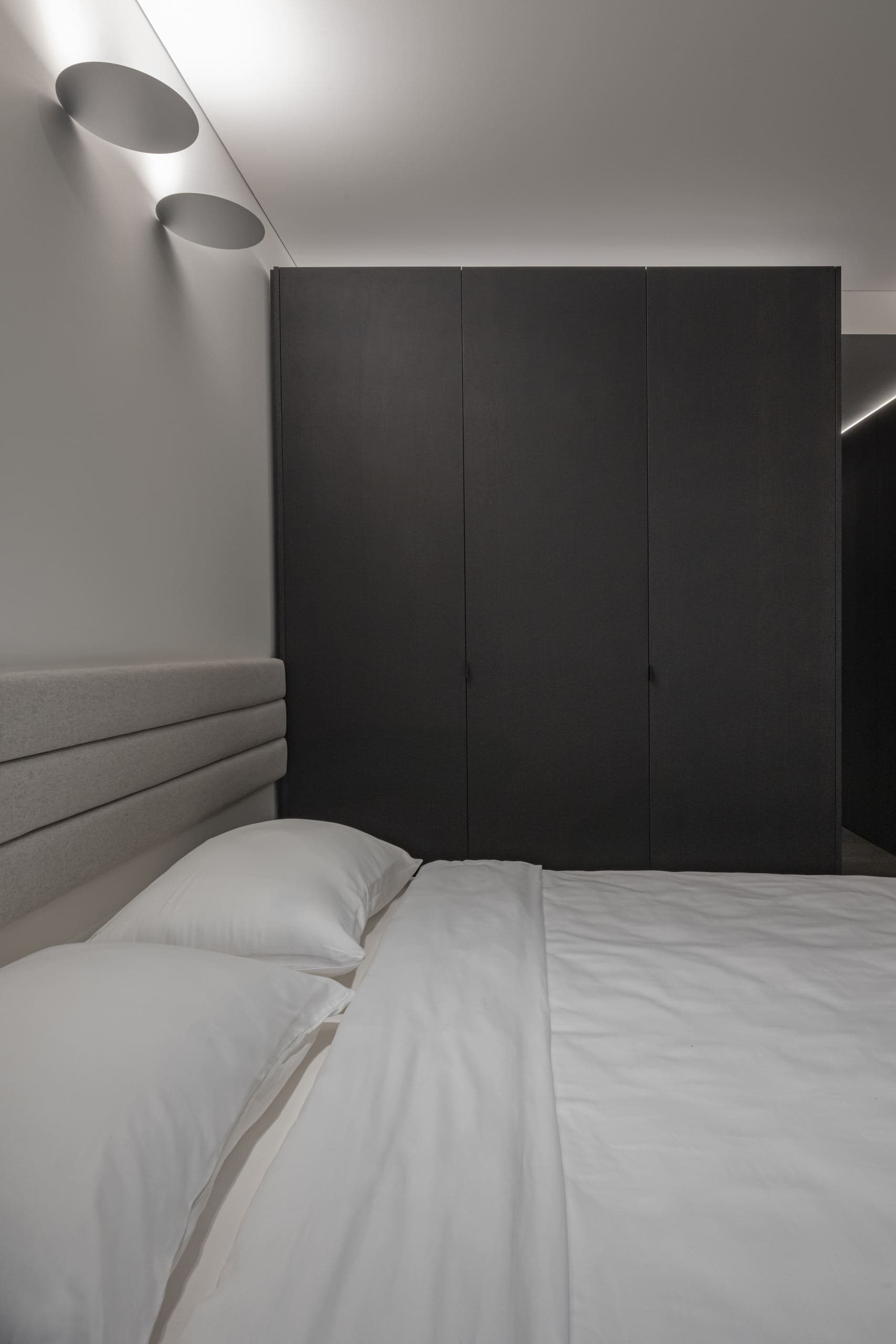 Paupys Apartment — bed beneath a wall light, the black headboard volume behind
