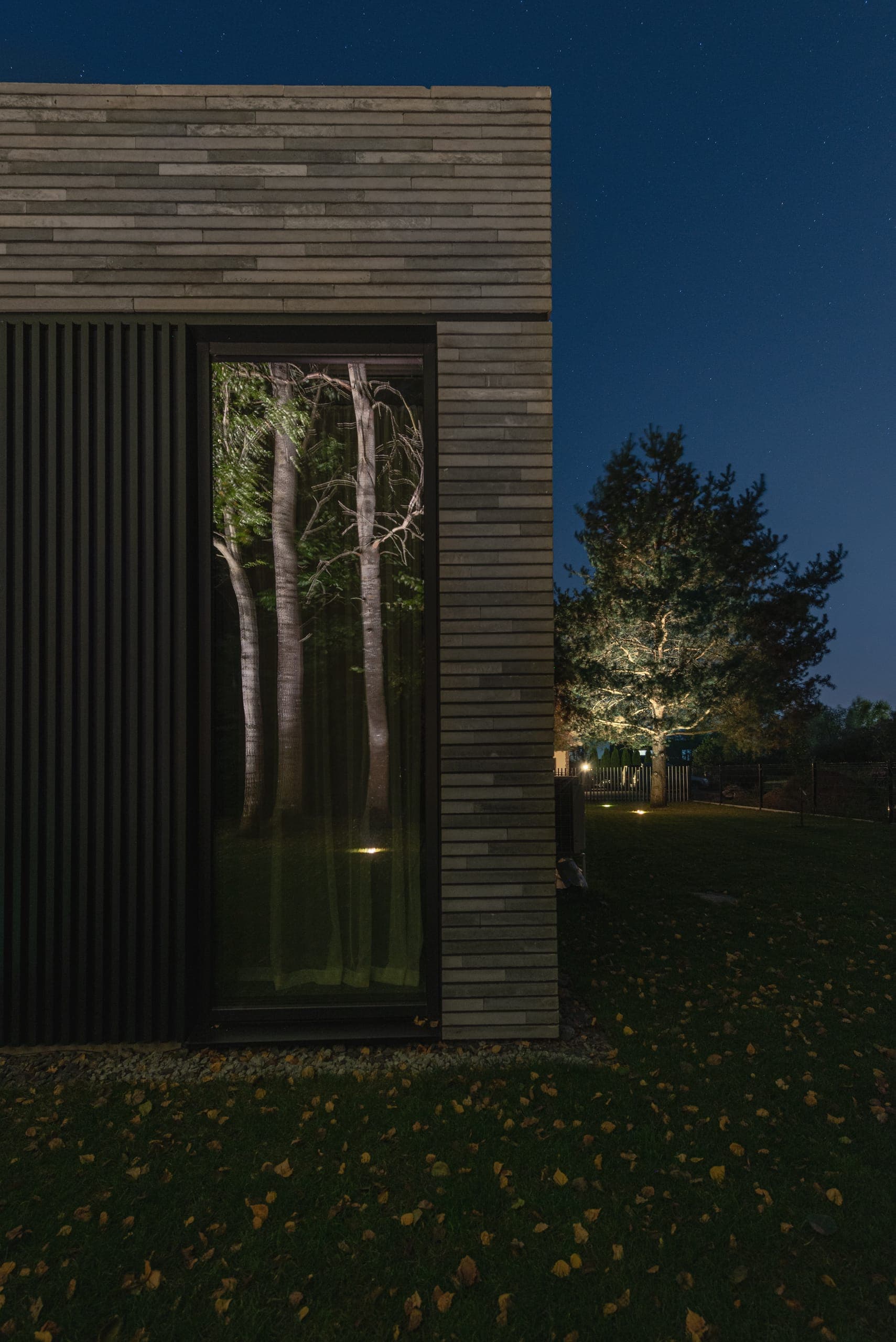 Modern Family House — tall window in the brick facade reflecting floodlit trees at night