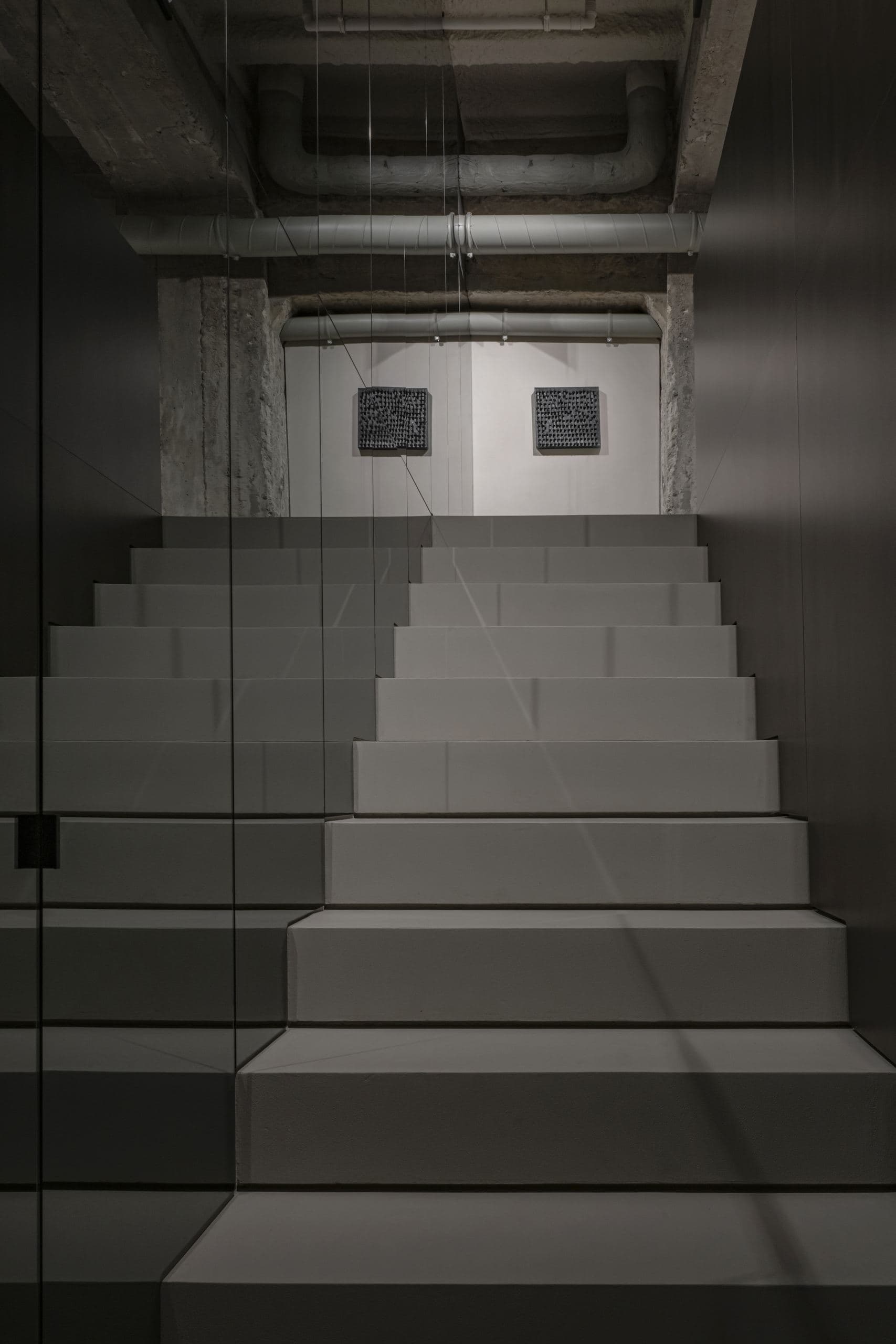 Loft Office — looking down a concrete stairwell past framed artwork to the lower level