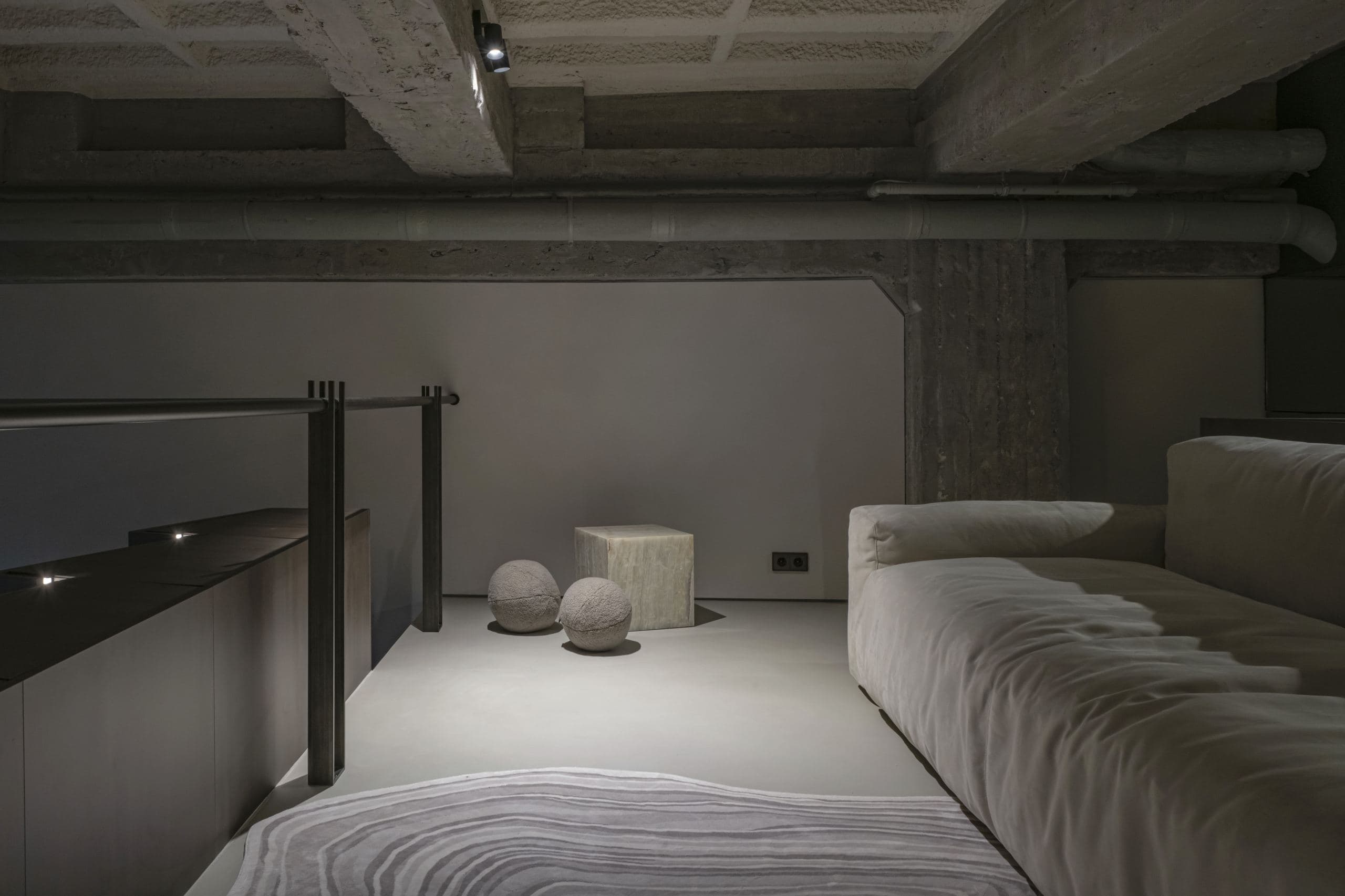 Loft Office — bed and round side tables beneath the exposed concrete-beam ceiling